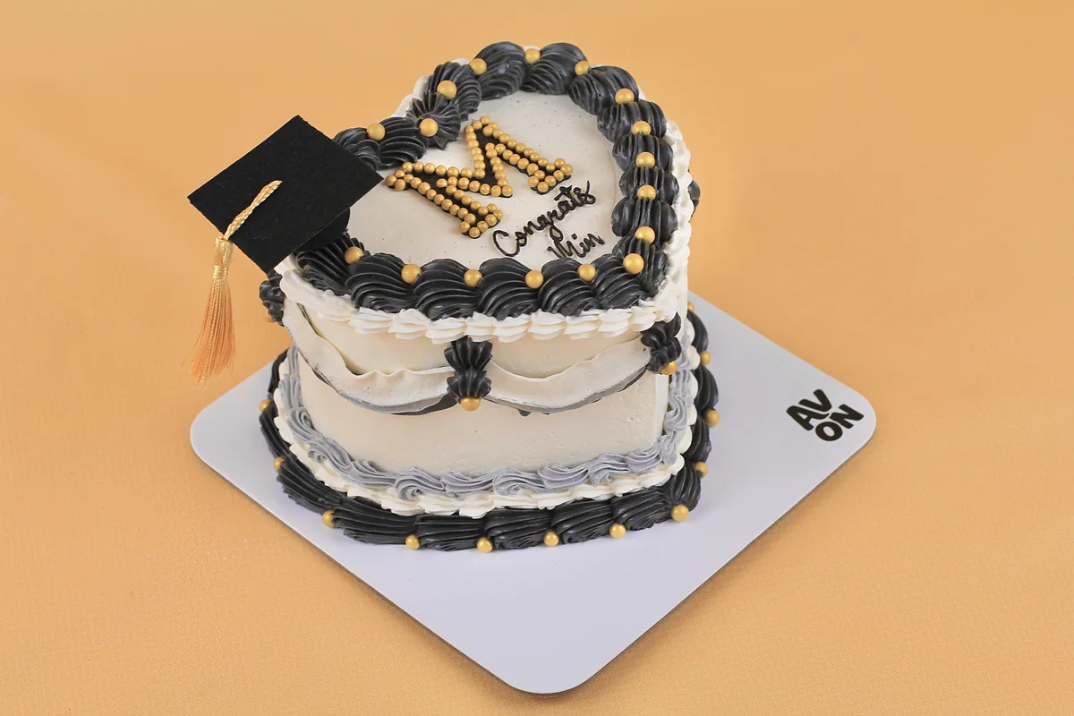 Black and white heart-shaped graduation cake with a gold letter M and a cap topper